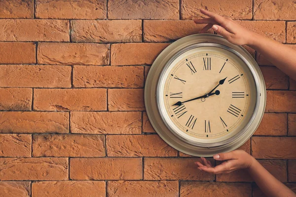 Female hands with clock on brick wall