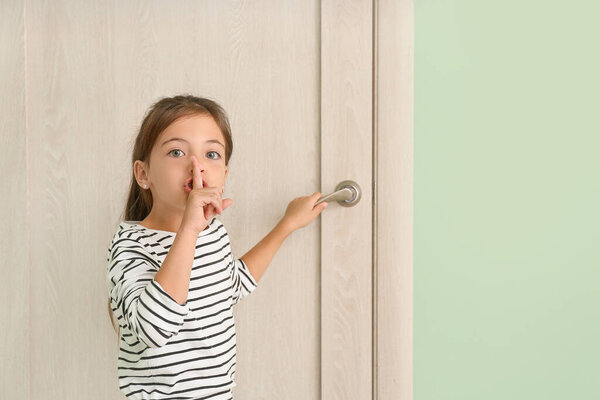 Симпатичная маленькая девочка показывает жест молчания возле закрытой двери