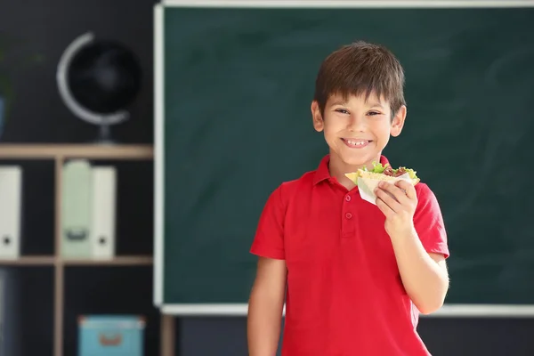 Schoolboy with sandwich against blurred background in school