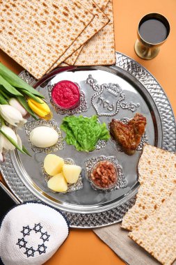 Passover Seder plate with traditional food and Jewish cap on color background clipart