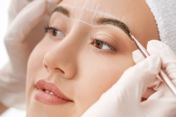 Young woman undergoing eyebrow correction procedure in beauty salon, closeup