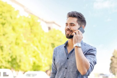 Modern kol saati olan yakışıklı bir adam dışarıda cep telefonuyla konuşuyor.
