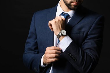 Koyu arkaplanda şık kol saati olan genç bir işadamı.