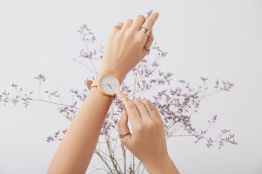 Şık kol saati ve açık arkaplanda çiçekleri olan kadın elleri.