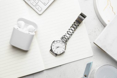 Hafif arkaplanda şık kol saati, defter ve kulaklıklar