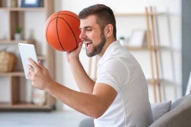Top ve tabletli genç adam evde spor bahisleri oynuyor.