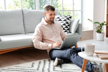 Evde dizüstü bilgisayarda çalışan genç adam.