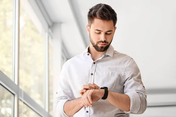 Handsome businessman looking at smart watch near window in room