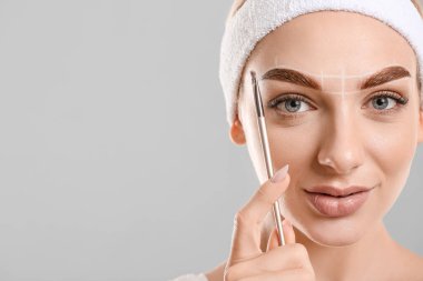 Gri arka planda kaşlarını düzelten genç bir kadın.