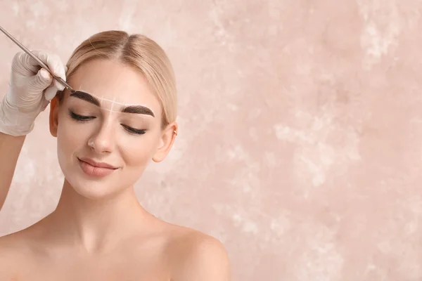 Young woman undergoing eyebrow correction procedure on color background