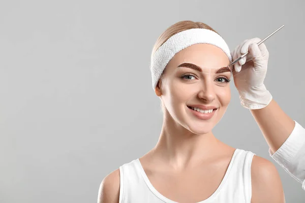 Mujer Joven Sometida Procedimiento Corrección Cejas Sobre Fondo Gris — Foto de Stock