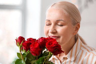 Evde bir buket güzel gül taşıyan olgun bir kadın.