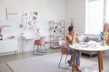 Stüdyoda çalışan bir fincan kahveli kadın moda tasarımcısı.