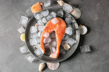 Koyu arkaplanda çiğ somon bifteği ve buz küpleriyle dolu bir tabak.