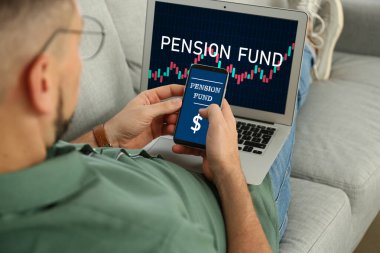 Cep telefonu ve dizüstü bilgisayarı olan bir adam evde emeklilik fonunun çevrimiçi hizmetini kullanıyor