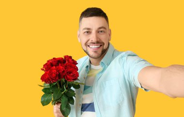 Güzel çiçeklerle dolu bir buketi olan yakışıklı adam arka planda selfie çekiyor.