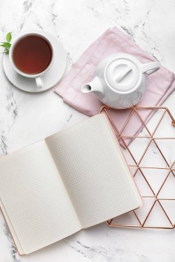 Çaydanlıklı kompozisyon, boş defter ve arka planda bir fincan çay.