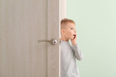 Şaşırmış küçük çocuk kapıdan dışarı bakıyor.