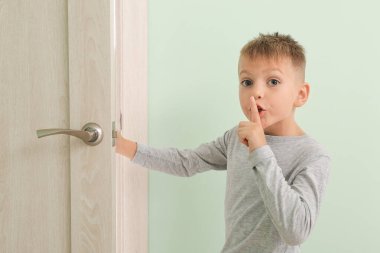 Sevimli küçük çocuk sessiz bir jest yapıyor ve odanın kapısını açıyor.
