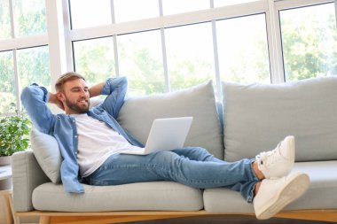 Bilgisayarlı genç adam evde dinleniyor.