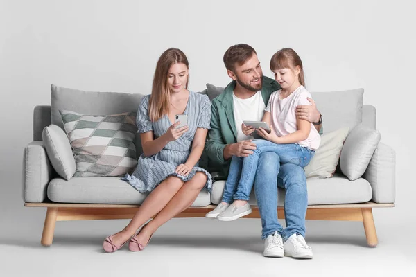Família Feliz Com Dispositivos Modernos Sofá Contra Fundo Claro — Fotografia de Stock