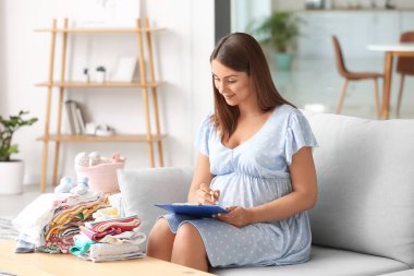 Evde bebek kıyafetleriyle güzel hamile bir kadın var.