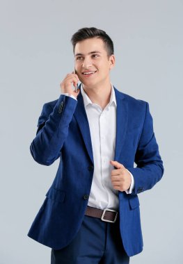Gri arka planda cep telefonuyla konuşan yakışıklı iş adamı