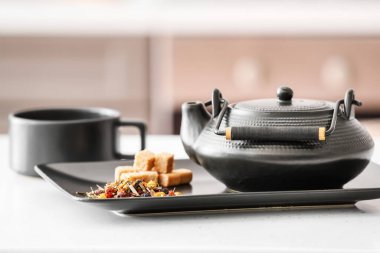 Süslü çaydanlık ve kuru çay yaprakları odadaki ışık masasında.