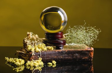 Kristal falcı küresi, kitap ve kuru otlar masada.