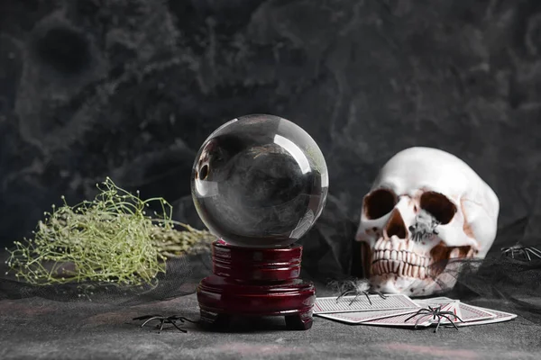 Koyu arkaplanda kristal falcı, kartlar ve insan kafatası.