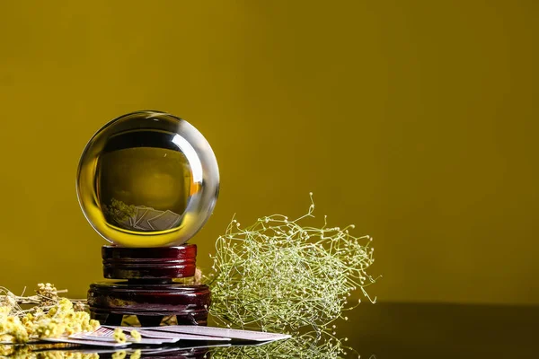 Kristal falcı küresi, kartlar ve kuru otlar masada.