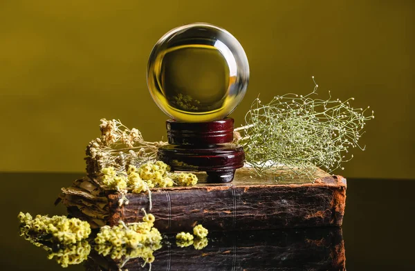 Kristal falcı küresi, kitap ve kuru otlar masada.