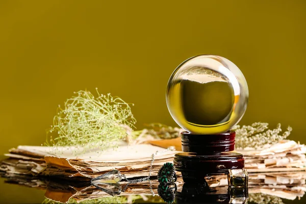 Kristal falcı küresi, kitap ve kuru otlar masada.