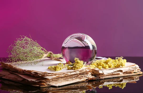 Kristal falcı küresi, eski kitap ve kuru otlar masada.