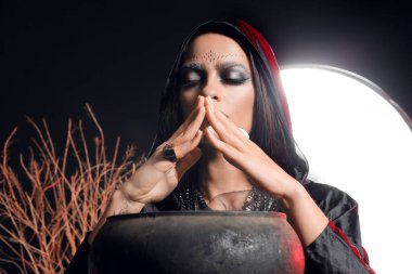 Kötü kalpli genç cadı karanlık arka planda ayin yapıyor.