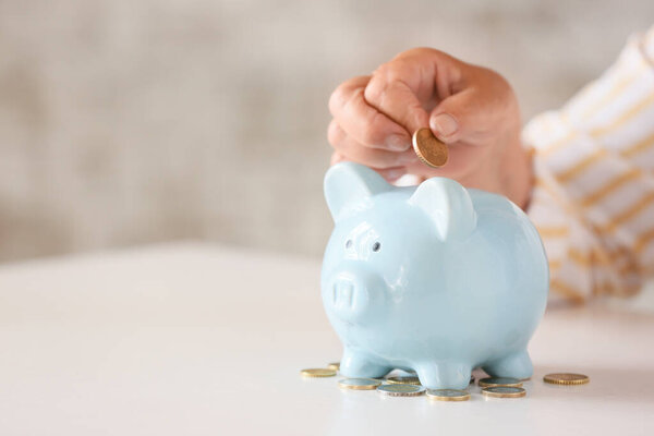 Старшая женщина кладет монету в копилку за столом. Концепция пенсионного обеспечения