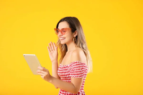 Young woman with tablet computer video chatting on color background