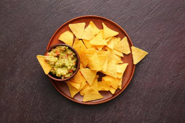 Koyu arkaplanda lezzetli nachos ve guacamole soslu tabak.