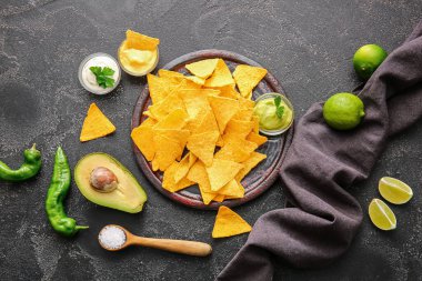 Koyu arkaplanda lezzetli nachos ve soslu tabak.