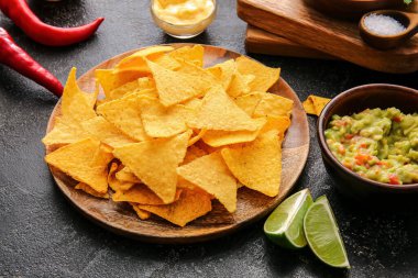 Koyu arkaplanda lezzetli nachos ve soslu tabak.