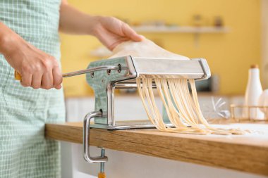 Mutfaktaki masada makineli makarna yapan kadın.