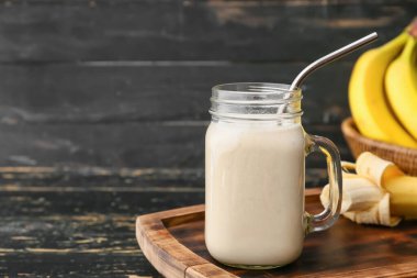 Ahşap arka planda lezzetli muzlu smoothie ile Mason kavanozu