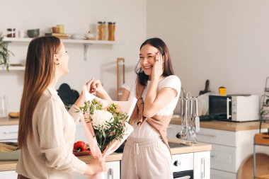 Genç bir kadın mutfakta kız arkadaşını selamlıyor.