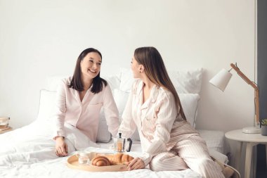 Genç lezbiyen çift yatakta kahvaltı yapıyor.