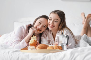 Genç lezbiyen çift yatakta kahvaltı yapıyor.