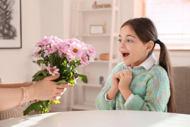 Şaşırmış küçük kız evde annesinden bir buket güzel çiçek alıyor.