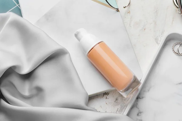 Bottle of makeup foundation and accessories on light background