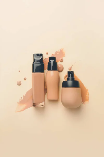 Bottles of makeup foundation and samples on color background