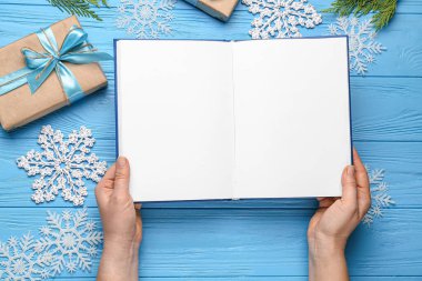 Boş kitabı olan kadın elleri ve renkli ahşap arka planda Noel dekoru