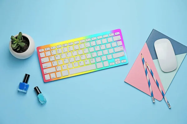Colorful computer keyboard with mouse, stationery and nail polishes on blue background